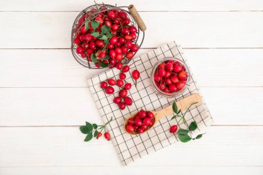 Kaşık ve kavanoz beyaz ahşap masada taze gül kalçası çilekleri.