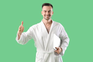 Bornozlu mutlu genç adam yeşil arka planda başparmağını gösteriyor.