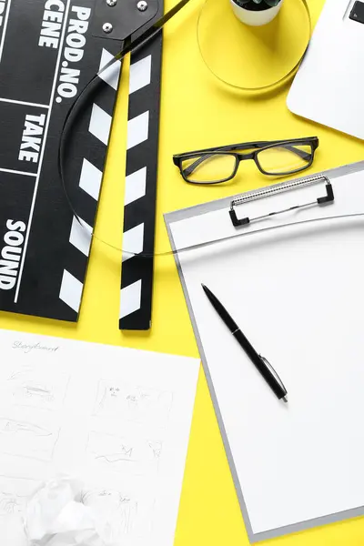 Clipboard with movie clapper and eyeglasses on yellow background