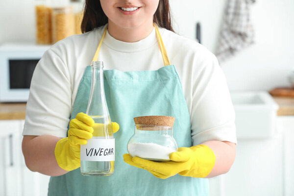 Woman with bottle of vinegar and baking soda in kitchen