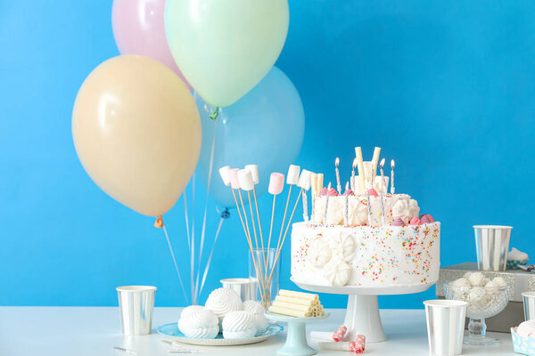 Торт на день рождения с различными сладостями на столе у голубой стены