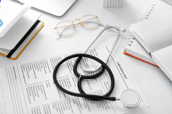Stethoscope with laboratory test and notebooks on white medical desk, closeup