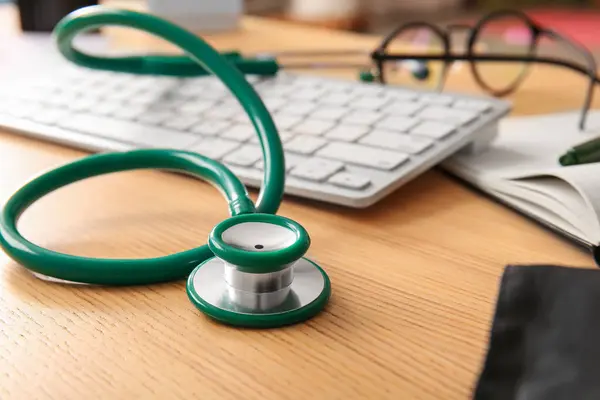 Stethoscope with computer keyboard on wooden medical desk, closeup