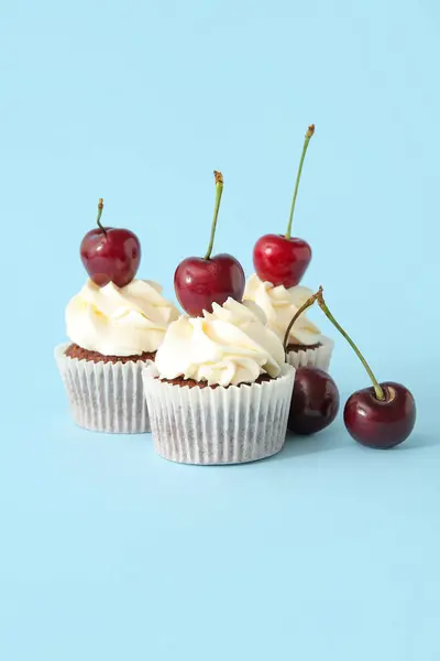 Tasty cherry cupcakes on blue background