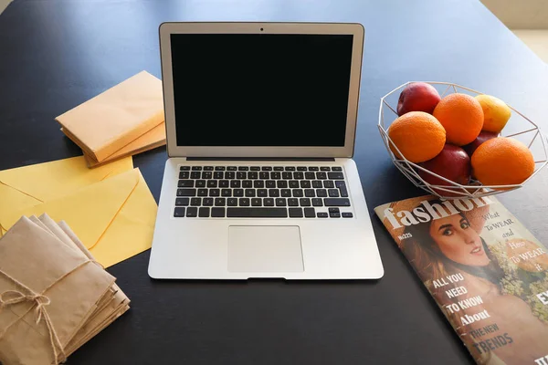 Blank laptop with fruits, magazine and letters on table in office