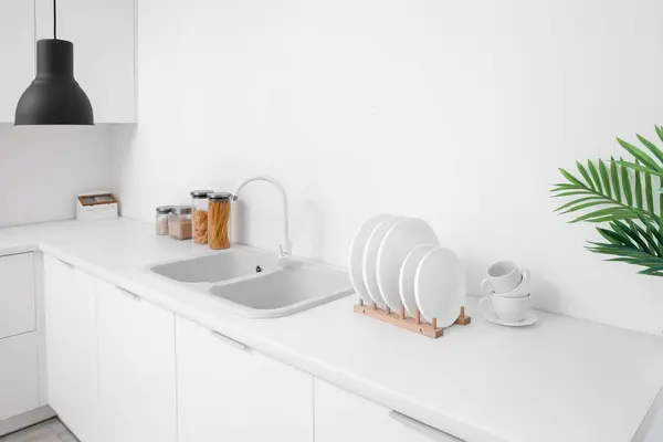 Holder with clean dishes near sink on counter in kitchen