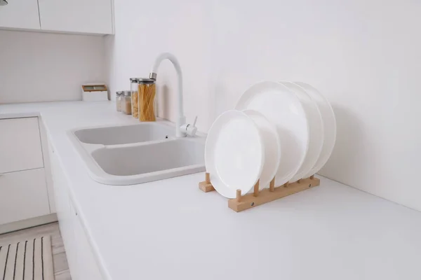 Holder with clean dishes near sink on counter in kitchen