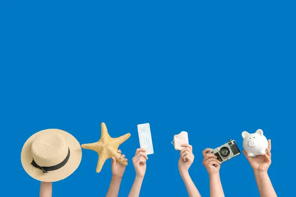 Female hands with hat, ticket, photo camera, piggy bank and wallet on blue background. Travel concept