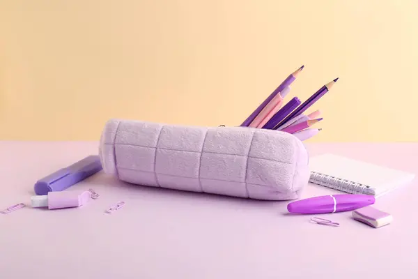 Purple pencil case with school stationery on color background