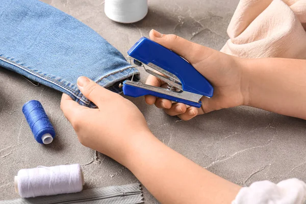 stock image Female hands with different supplies sewing jeans on grunge grey background