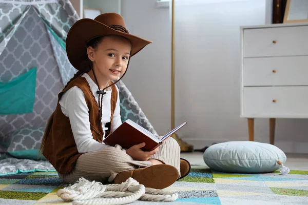 Cute little cowgirl reading adventure book at home