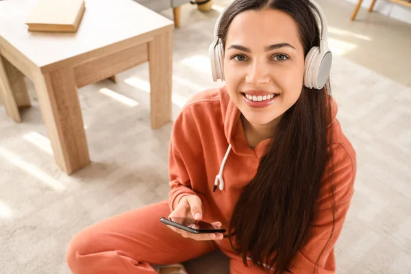 Young woman in hoodie with headphones using mobile phone at home
