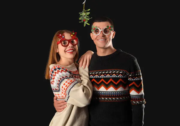 Young couple with mistletoe branch on dark background