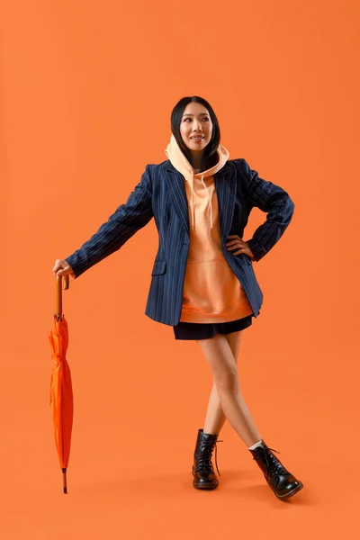 オレンジ色の背景に傘を持つフーディーの若いアジアの女性 — ストック写真