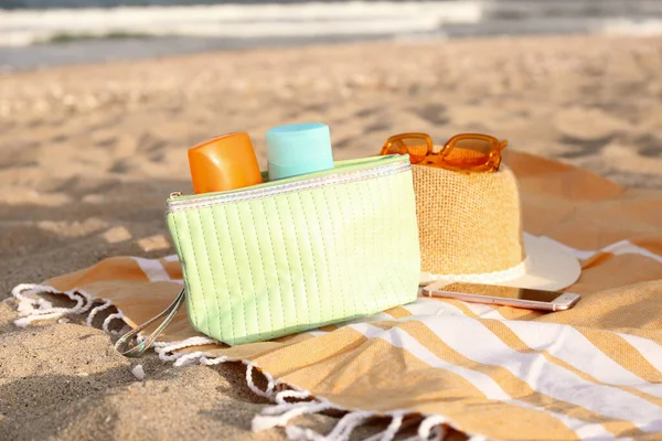 Cosmetic bag with bottles of sunscreen cream and hat on sand