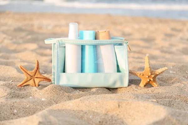 Cosmetic bag with bottles of sunscreen cream and starfishes on sand
