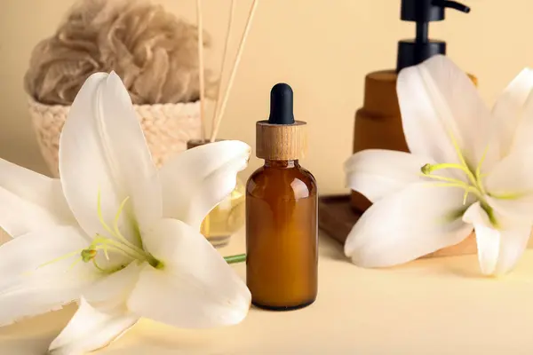 Bottle of essential oil, spa accessories and lily flowers on color background