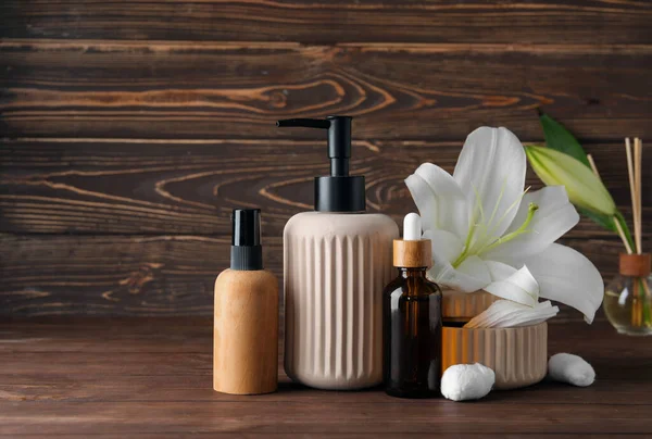 Bottles of cosmetic products, cotton pads and lily flowers on wooden background