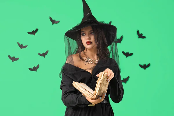 Young witch with spell book and bats on green background