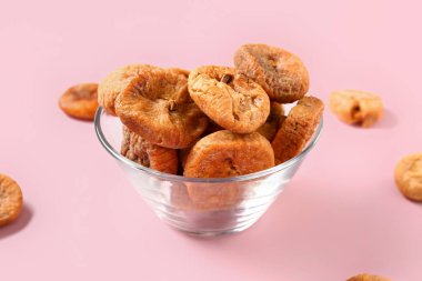 Pembe arka planda kurutulmuş incirli cam kase.