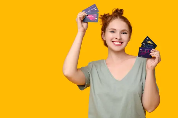 Beautiful young woman with credit cards on yellow background