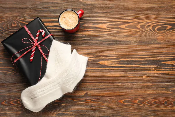 Warm socks with Christmas gift and cup of coffee on wooden background
