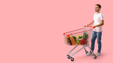 İnsan ve alışveriş arabası pembe arka planda ürünlerle dolu ve metin için yeri var.