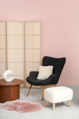 Tahta sehpası olan koltuk, puf ve tuvalet perdesi pembe duvarın yanında.