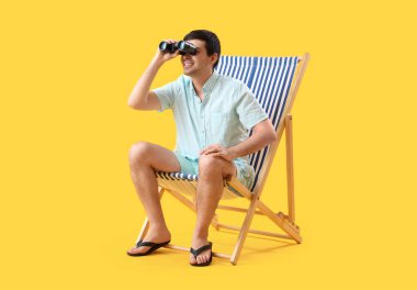 Sarı arka planda, güvertede oturan dürbünlü genç adam.