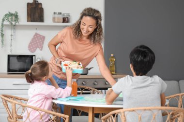 Anne mutfakta küçük çocuklarına beslenme çantası veriyor.