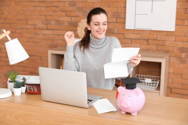 Domuz kumbarasında oturmuş mektup okuyan mutlu bir kız öğrenci. Öğrenci kredisi kavramı