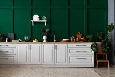 Modern mutfakta okaliptüs dalları, şarap şişesi ve mutfak aletleri olan beyaz tezgah.