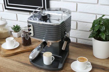 Modern coffee machine with cups of hot espresso on table in kitchen