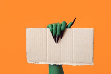 Turuncu arka planda boş kağıt çarşaf ile cadının yeşil eli. Cadılar Bayramı