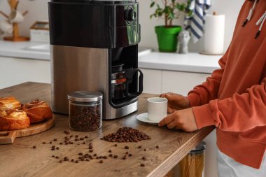 Modern kahve makinesinin yanında fincanı olan kadın mutfaktaki masada.