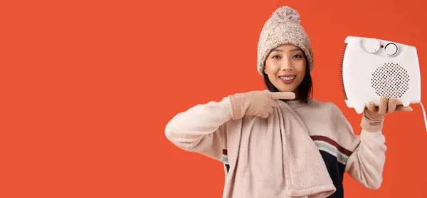 テキスト用のスペースを持つオレンジ色の背景に電気ファンヒーターを保持する若いアジアの女性 ヒーティングシーズン — ストック写真