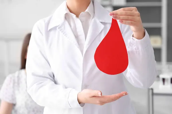 Female doctor with paper blood drop in clinic, closeup