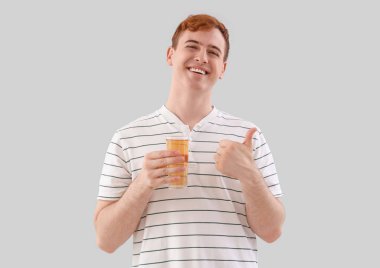 Elinde bir bardak meyve suyu olan genç adam arka planda baş parmağını kaldırıyor.
