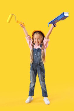 Sarı arka planda boya silindiri olan şirin bir müteahhit kız.