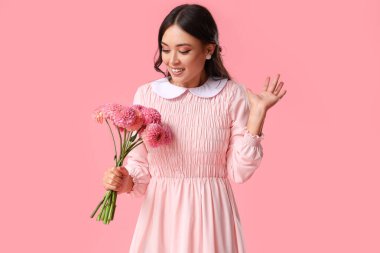 Pembe arka planda bir buket yıldız çiçeğiyle güzel bir Asyalı kadın.