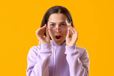 Sarı arka planda leylak kapüşonlu ve güneş gözlüklü genç kadın, yakın plan.