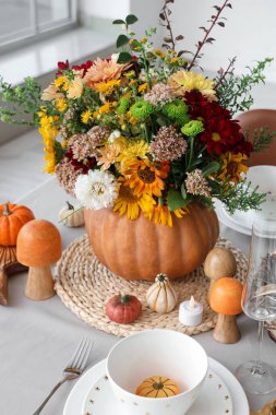 Şenlikli yemek masasında, balkabağında farklı sonbahar çiçeklerinden bir buket.