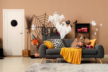 Sonbahar kıyafetleri içinde korkunç Cadılar Bayramı iskeleti hediye kutusu ve oturma odasındaki kanepede oturan tarantula.