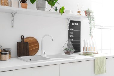 Modern mutfağın içinde lavabo ve çatal bıçaklarla dolu beyaz tezgahlar.