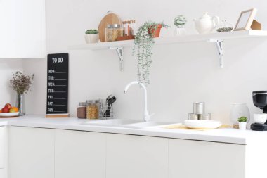 Beyaz tezgahlı, raflı, lavabolu ve çatallı bir mutfak.