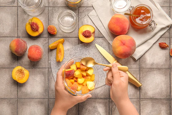 Woman preparing sweet peach jam on grey tile background