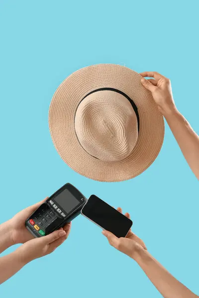Women with mobile phone, payment terminal and hat on blue background