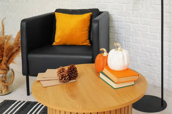 Pumpkins with books and fir cones on table in living room