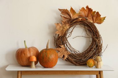 Kabaklı masa, çelenk ve sonbahar yaprakları oturma odasındaki beyaz duvarın yanında.