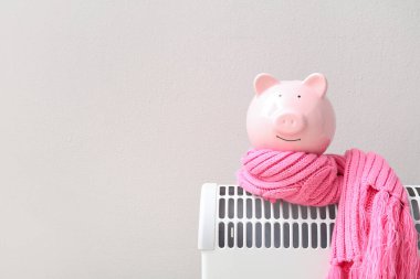 Evdeki beyaz duvarın yanında elektrikli konteyner ısıtıcısında sıcak atkı olan domuz kumbarası. Isıtma kaydetme kavramı